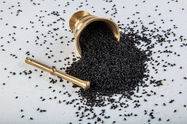 Nigella sativa tohumları ayrıca siyah kimyon, kalo jeera, kalonji ve siyah karanfil olarak da bilinir demir kepçesinde ve beyaz ahşap zemin üzerinde havan ve kopyalama alanı ile birlikte.