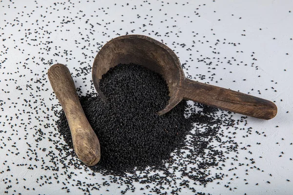 Nigella sativa tohumları ayrıca siyah kimyon, kalo jeera, kalonji ve siyah karanfil olarak da bilinir demir kepçesinde ve beyaz ahşap zemin üzerinde havan ve kopyalama alanı ile birlikte.