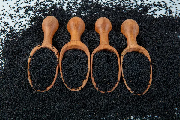 Black cumin seeds - natural antioxidant. Black cumin seeds essential oil with wooden spoon or shovel on wooden background. Organic herbal medicine for many diseases.