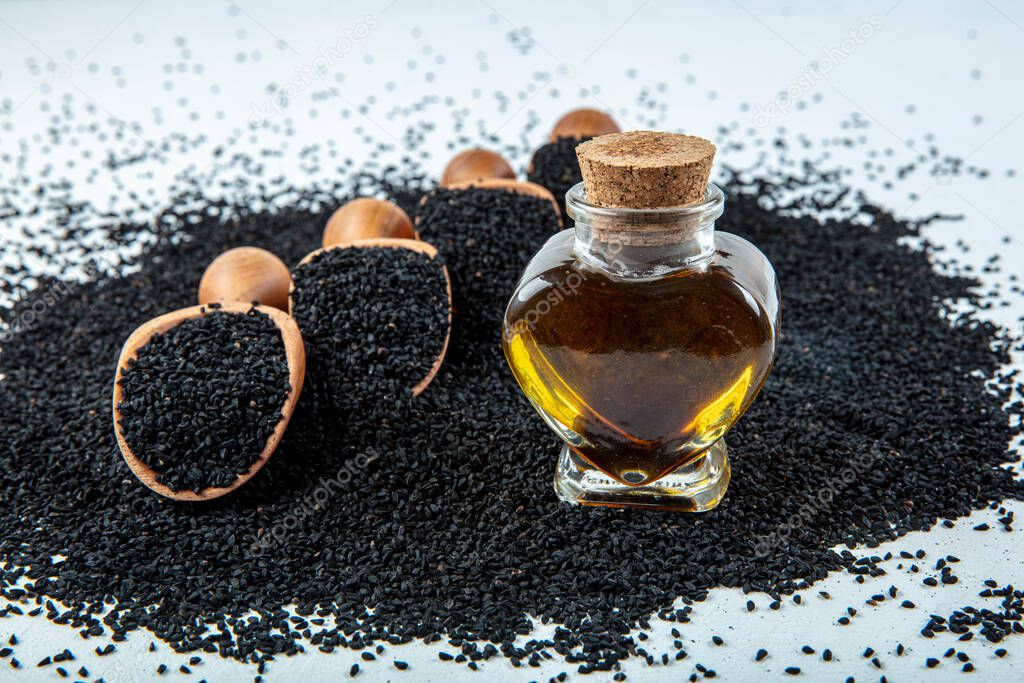 Black cumin seeds - natural antioxidant. Black cumin seeds essential oil with wooden spoon or shovel on wooden background. Organic herbal medicine for many diseases.