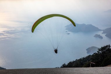 Gökyüzünde paraşütle atlıyor. Paraglider gün batımında dağlarla birlikte denizin üzerinde uçuyor. Oludeniz, Babadag, Mugla, Türkiye 'deki Paraşütçü ve Mavi Göl manzarası.
