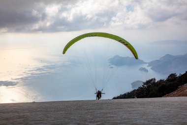Gökyüzünde paraşütle atlıyor. Paraglider gün batımında dağlarla birlikte denizin üzerinde uçuyor. Oludeniz, Babadag, Mugla, Türkiye 'deki Paraşütçü ve Mavi Göl manzarası.