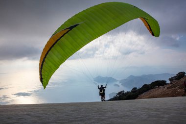 Gökyüzünde paraşütle atlıyor. Paraglider gün batımında dağlarla birlikte denizin üzerinde uçuyor. Oludeniz, Babadag, Mugla, Türkiye 'deki Paraşütçü ve Mavi Göl manzarası.