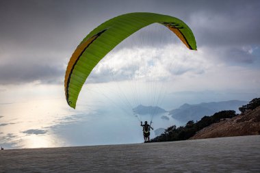 Gökyüzünde paraşütle atlıyor. Paraglider gün batımında dağlarla birlikte denizin üzerinde uçuyor. Oludeniz, Babadag, Mugla, Türkiye 'deki Paraşütçü ve Mavi Göl manzarası.