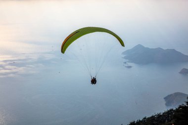 Gökyüzünde paraşütle atlıyor. Paraglider gün batımında dağlarla birlikte denizin üzerinde uçuyor. Oludeniz, Babadag, Mugla, Türkiye 'deki Paraşütçü ve Mavi Göl manzarası.