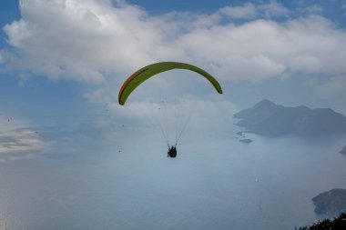 Gökyüzünde paraşütle atlıyor. Paraglider gün batımında dağlarla birlikte denizin üzerinde uçuyor. Oludeniz, Babadag, Mugla, Türkiye 'deki Paraşütçü ve Mavi Göl manzarası.
