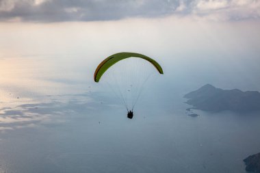 Gökyüzünde paraşütle atlıyor. Paraglider gün batımında dağlarla birlikte denizin üzerinde uçuyor. Oludeniz, Babadag, Mugla, Türkiye 'deki Paraşütçü ve Mavi Göl manzarası.