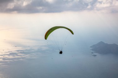Gökyüzünde paraşütle atlıyor. Paraglider gün batımında dağlarla birlikte denizin üzerinde uçuyor. Oludeniz, Babadag, Mugla, Türkiye 'deki Paraşütçü ve Mavi Göl manzarası.