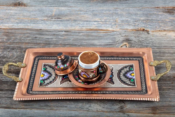 Turkish coffee. Pouring Turkish coffee into vintage cup on wooden background. Pouring Turkish coffee into traditional embossed metal cup.