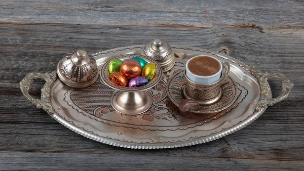 Pouring Turkish coffee into vintage cup on wooden background. Turkish coffee in a copper Turks and grains are scattered on the wooden surface.