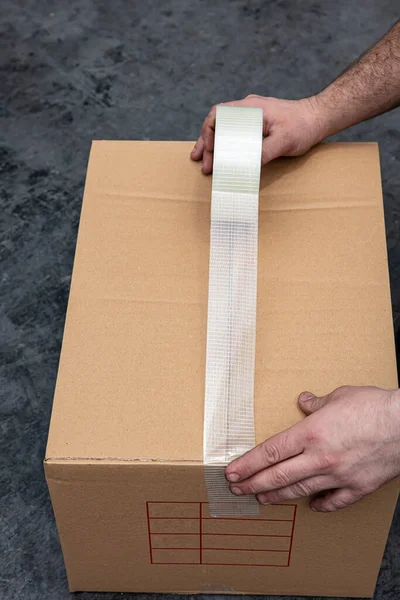 Packing Boxes with Tape. Sticking duct tape to a Kraft cardboard box. close-up of sealing cardboard box with duct tape.
