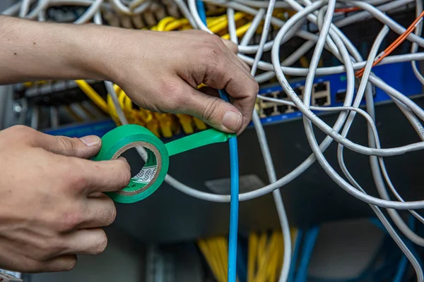 Electrician is repairing the wiring in the electrical room with electrical tape. Cropped view of electrician using insulating tape while fixing wires of electric panel.