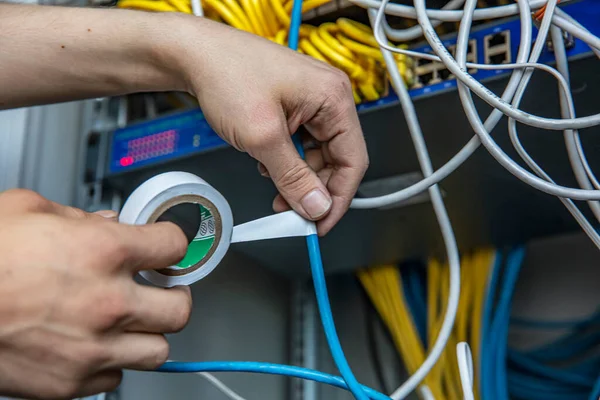 Electrician is repairing the wiring in the electrical room with electrical tape. Cropped view of electrician using insulating tape while fixing wires of electric panel.