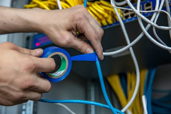 Electrician is repairing the wiring in the electrical room with electrical tape. Cropped view of electrician using insulating tape while fixing wires of electric panel.