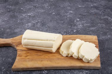 Fresh butter block sliced on wooden cutting board against table.