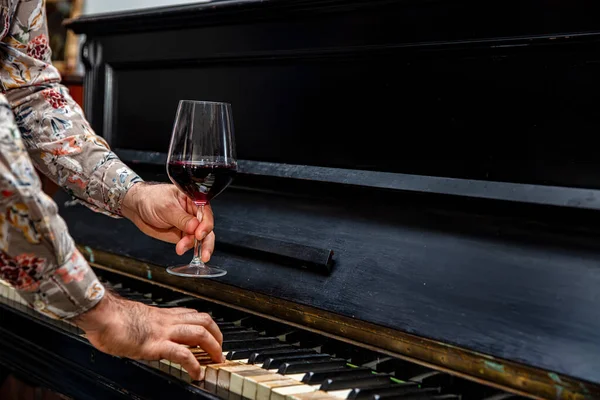 Old classical piano keys and Wine glass. a glass of red burgundy wine in an elegant etched wine glass resting on a piano keyboard.