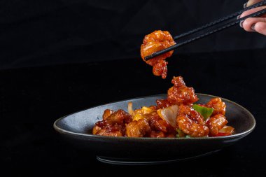 Mançurya usulü kızarmış tavuk parçaları, dolmalık biber ve soğanla pişirilmiş ve koyu baharatlı sosla kaplanmış. Asya 'dan esinlenilmiş Hint-Çin mutfağı karanlık arka planda, yakın plan yemek fotoğrafçılığında modern bir kâsede servis edilir..