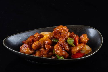 Mançurya usulü kızarmış tavuk parçaları, dolmalık biber ve soğanla pişirilmiş ve koyu baharatlı sosla kaplanmış. Asya 'dan esinlenilmiş Hint-Çin mutfağı karanlık arka planda, yakın plan yemek fotoğrafçılığında modern bir kâsede servis edilir..