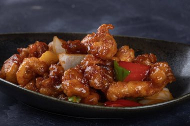 Mançurya usulü kızarmış tavuk parçaları, dolmalık biber ve soğanla pişirilmiş ve koyu baharatlı sosla kaplanmış. Asya 'dan esinlenilmiş Hint-Çin mutfağı karanlık arka planda, yakın plan yemek fotoğrafçılığında modern bir kâsede servis edilir..