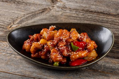 Mançurya usulü kızarmış tavuk parçaları, dolmalık biber ve soğanla pişirilmiş ve koyu baharatlı sosla kaplanmış. Asya 'dan esinlenilmiş Hint-Çin mutfağı karanlık arka planda, yakın plan yemek fotoğrafçılığında modern bir kâsede servis edilir..