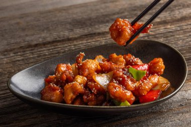 Mançurya usulü kızarmış tavuk parçaları, dolmalık biber ve soğanla pişirilmiş ve koyu baharatlı sosla kaplanmış. Asya 'dan esinlenilmiş Hint-Çin mutfağı karanlık arka planda, yakın plan yemek fotoğrafçılığında modern bir kâsede servis edilir..