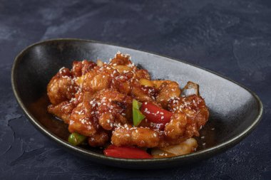 Mançurya usulü kızarmış tavuk parçaları, dolmalık biber ve soğanla pişirilmiş ve koyu baharatlı sosla kaplanmış. Asya 'dan esinlenilmiş Hint-Çin mutfağı karanlık arka planda, yakın plan yemek fotoğrafçılığında modern bir kâsede servis edilir..