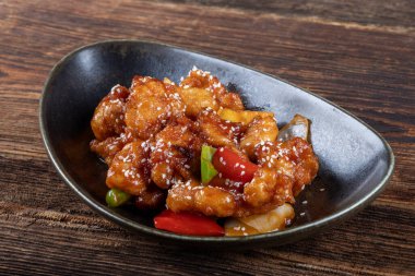 Mançurya usulü kızarmış tavuk parçaları, dolmalık biber ve soğanla pişirilmiş ve koyu baharatlı sosla kaplanmış. Asya 'dan esinlenilmiş Hint-Çin mutfağı karanlık arka planda, yakın plan yemek fotoğrafçılığında modern bir kâsede servis edilir..