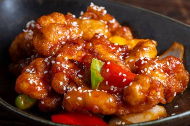Mançurya usulü kızarmış tavuk parçaları, dolmalık biber ve soğanla pişirilmiş ve koyu baharatlı sosla kaplanmış. Asya 'dan esinlenilmiş Hint-Çin mutfağı karanlık arka planda, yakın plan yemek fotoğrafçılığında modern bir kâsede servis edilir..