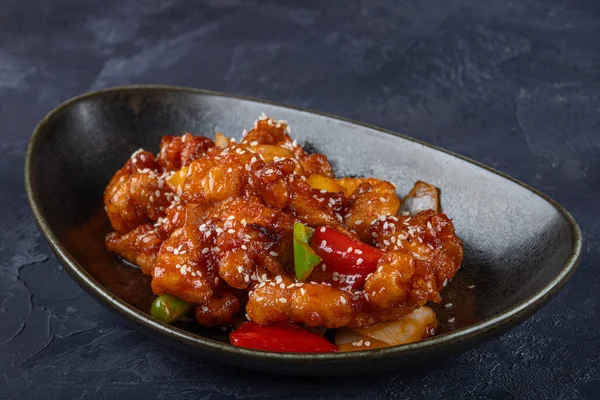 Mançurya usulü kızarmış tavuk parçaları, dolmalık biber ve soğanla pişirilmiş ve koyu baharatlı sosla kaplanmış. Asya 'dan esinlenilmiş Hint-Çin mutfağı karanlık arka planda, yakın plan yemek fotoğrafçılığında modern bir kâsede servis edilir..