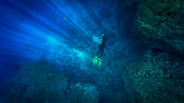 Underwater photo of scuba diving adventure with rays of light in the deep blue ocean.