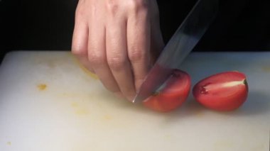 Bir insanın elleri mutfak bıçağı kullanarak kesme tahtasında taze kırmızı domates kesiyor.