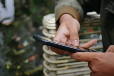 Koi ile Göl kenarında akıllı telefon kullanan kişi.