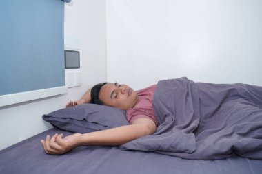 Bir adam kapsül bir otel yatağında, yorulmuş, dağınık bir şekilde uyur..