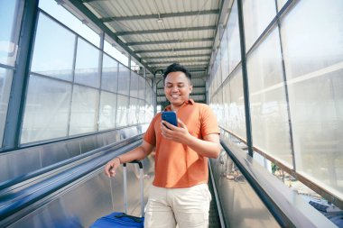 Havaalanındaki Transit Hub 'daki yürüyen merdivende akıllı telefon kullanan adam.