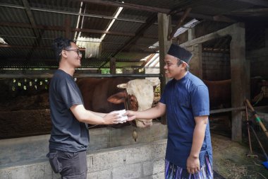 Asyalı erkek çiftçi, limuzin ineği alışverişini tamamladıktan sonra bir alıcıyla tokalaşıyor.