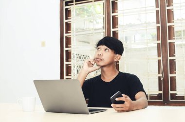 Asyalı adam ciddi bir ifadeyle dizüstü bilgisayarın önünde oturuyor.