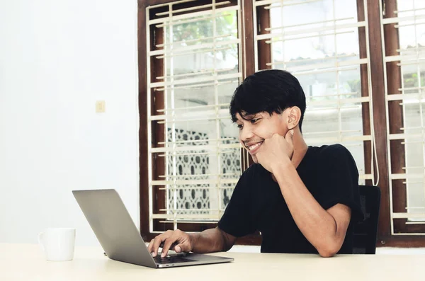 Dizüstü bilgisayarın önünde oturan Asyalı bir adam bir ödev üzerinde çalışıyor.