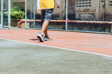 Genç adam tenis kortunda yürüyor.