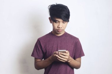 Genç Asyalı adam beyaz arka planda telefonuyla meşgul.