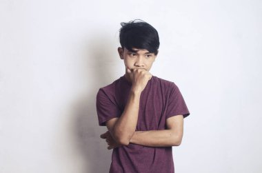 Beyaz bir arka planda kafası karışık ve düşünceli genç bir Asyalı.