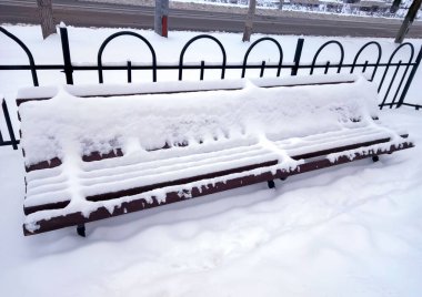 Kışın şehir parkında çok kar yağan bankta. Bankta çok kar var. Güzel kış manzarası.