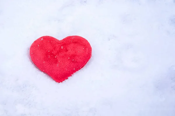 Red plush heart, lying in winter on the white pure snow in the sun. Love the concept of Valentine\'s Day. Lost heart top view. Valentine\'s day background with space to copy.