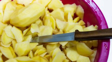 Dilimlenmiş çiğ patates ve plastik bir kasede beyaz arka planda yakın plan çekilmiş bir bıçak..