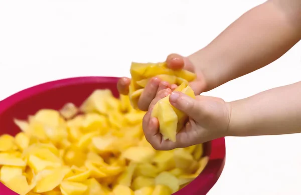 Mutlu bir çocuk, beyaz arka planda pembe bir kasede kesilmiş çiğ bir patatesi parçalara ayırır. Küçük bir çocuk yiyecekle oynar. Mutlu çocukluk kavramı. 