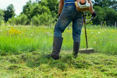 Adamın biri arka bahçede çim biçme makinesiyle çimleri biçiyor. Bahçıvan bir budama makinesiyle bahçedeki çimlerin üzerinde uzun çimleri biçer. Bir çiftçinin yaşam tarzı. Seçici odaklanma. Boşluğu kopyala.