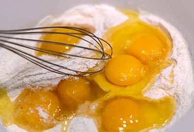 Un içinde taze çiğ tavuk yumurtası. Kırık çiğ yumurta ve buğday ununu hamur yapmak için çırpıcıyla karıştır. Yemek arkaplanı. Yumurtaların arka planı. Sağlıklı beslenme kavramı. Doğal arkaplan.