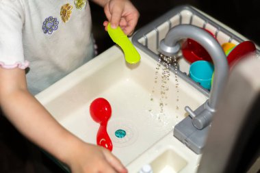 Çocukların mutfağında bir çocuk oynuyor. Bebek lavaboda plastik bulaşıkları yıkıyor, çocukların bağımsızlığını kazanıyor ve Montessori anaokulunda annelere yardım ediyor. Mutlu bir çocukluk. Eğitim Oyunları