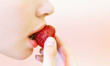 Tatlı çilek yiyen bir kız. Elinde büyük bir çilek tutan genç bir kızın resmi ve onu pembe bir arka planda ısırıyor ve mesaj atmak için boş bir alanı var. Güzel, doğal arka plan