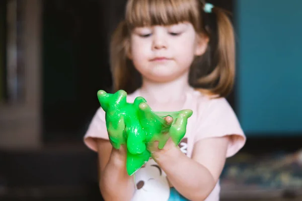 子供の手に緑のスライム 女の子がスライムで遊んでいる 子供は指を通して緑の粘菌を絞り出す 子供のゲーム 幸せな楽しい子供時代の概念 ストック画像