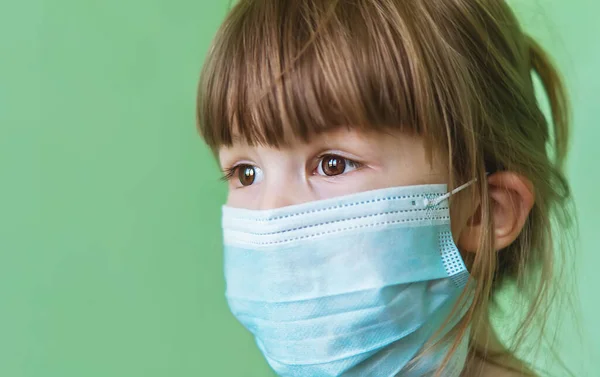 緑の背景の医療マスクの悲しい少女 子供の顔に使い捨て医療用マスク 疫学中の保護医療用マスクの子供 ウイルスや感染症からの保護 — ストック写真